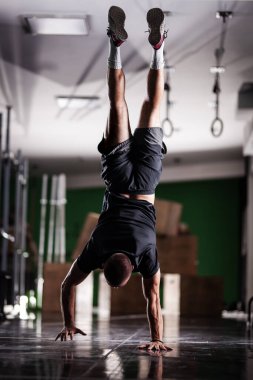 Ayakta duran ve baş aşağı yürüyen kaslı bir sporcu.