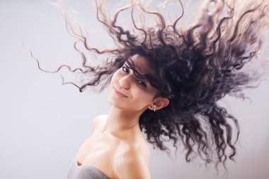 Havada uzun kıvırcık saçlı güzel esmer kız, stüdyo portresi. Mutlu gülen yüz ifadesi.