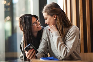 Bir kafede gülümseyen ve birbirine bakan iki bayan arkadaş.