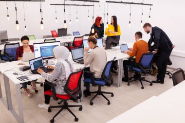 Group of multiethnic colleagues working on desktop computers in a modern office space. clipart