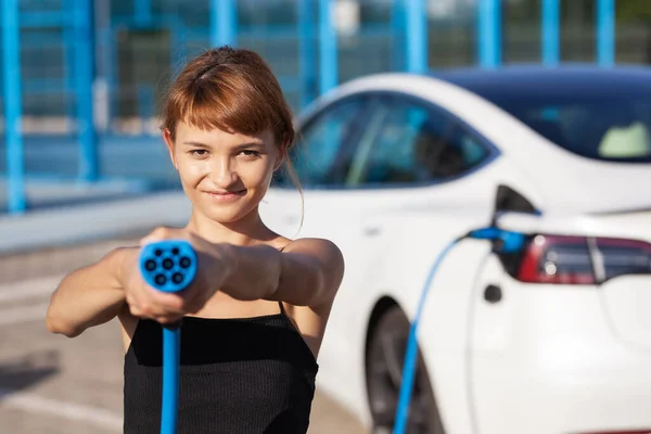 Gyönyörű Fiatal Lány Egy Elektromos Autó Mellett Töltőkábel Elhelyezése Tartása — Stock Fotó