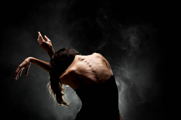 Half silhouette modern ballet dancer posing on dark background with smoke