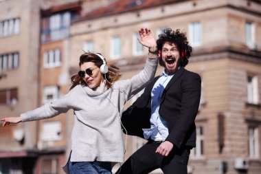 Genç iş arkadaşları işten sonra kulaklıkla dans ediyorlar. Mutlu arkadaşlar hoplayıp zıplıyorlar.