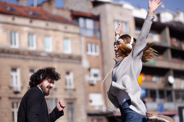 仕事の後にヘッドフォンで踊る若いビジネスの同僚 幸せな友達は屋外で飛び回って遊んでいます — ストック写真