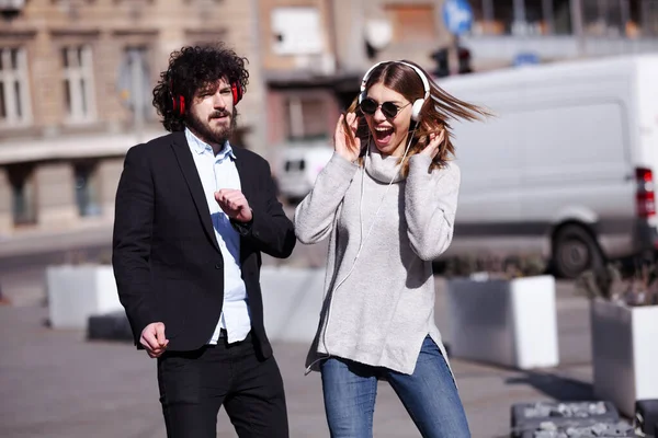 Genç iş arkadaşları işten sonra kulaklıkla dans ediyorlar. Mutlu arkadaşlar hoplayıp zıplıyorlar.