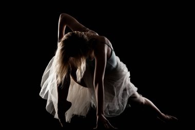 Siyah arka planda poz veren beyaz elbiseli bir balerin. yan aydınlatma silueti