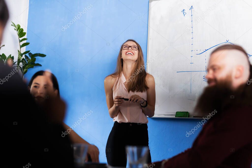Business people having a creative meeting. Successful multiethnic multiracial colleagues in an office. Smiling businesswoman standing at wall board with graphs.