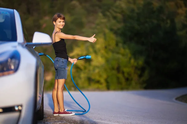 Elektrikli Arabanın Yanında Duran Bir Kız Şarj Kablosu Tutuyor Otostop — Stok fotoğraf