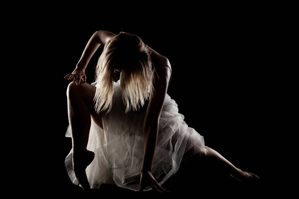 Ballerina with a white dress and black top posing on black background. side lit silhouette