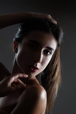 Güzel esmer kız stüdyo resmi. Koyu arkaplanda yarım siluet var. Ciddi yüz ifadesi.