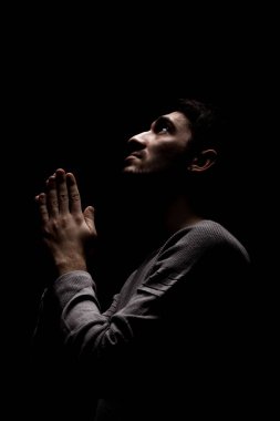 Karanlık odada dua eden kendinden emin bir gencin vesikalığı. Yukarıdan aydınlat ve yukarı bak..
