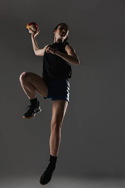Handball player posing on gray background. Girl jumping with ball.