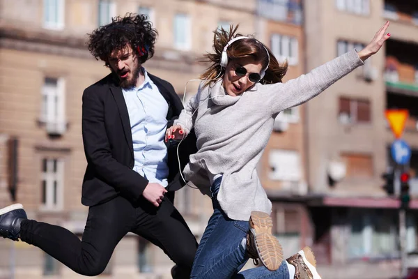 仕事の後にヘッドフォンで踊る若いビジネスの同僚 幸せな友達は屋外で飛び回って遊んでいます — ストック写真