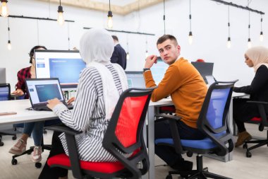 Modern bir ofis alanında masaüstü bilgisayarları üzerinde çalışan bir grup çok ırklı iş arkadaşı. Ayakları masada dinlenen bir kız.