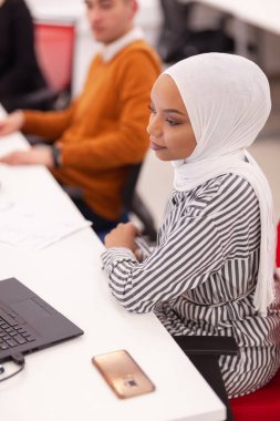 Laptop üzerinde çalışan tesettürlü Afrikalı Müslüman kız. Modern ofisteki çok ırklı çalışma arkadaşları.