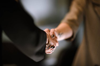 Two individuals are shaking hands in a professional setting, marking a successful agreement or greeting during a meeting in a modern office environment.