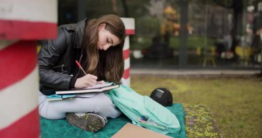 Focused Teen Girl Student Writing in Notebook in City Park During Autumn - Educational Aspirations and Creative Inspiration
