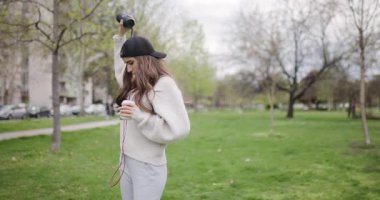 Young Woman Enjoys Music and Coffee in the Park While Using a Portable Speaker and Headphones