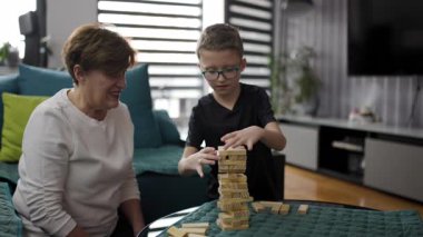 Grandmother and grandson are playing a game together. They are smiling and happy to spend time together. The boy is wearing glasses.