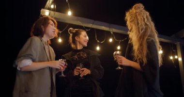 Arkadaşlar gece terasta içki içip sohbet etmekten zevk alıyorlar. Sıcak ışık samimi ve samimi bir atmosfer yaratıyor..