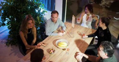 Arkadaşlar bir masanın etrafında toplanır, kadehlerini kaldırır ve mum ışığında kadeh kaldırırlar..