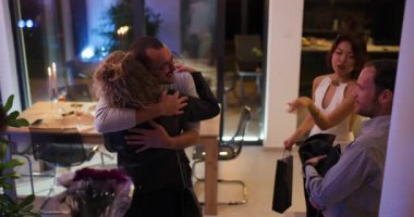 Arkadaşlar bir akşam yemeği partisine gelir ve ev sahiplerini kucaklayarak, çiçeklerle ve hediyelerle karşılarlar. Sıcak selamlar ve mutlu gülücükler.