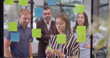 Kafkas iş adamlarından oluşan bir ekip yapışkan notlarla cam duvarın yanında duruyor. Renkli çıkartmalı Scrum metodolojisi. İş arkadaşları proje fikirlerini tartışıyor.