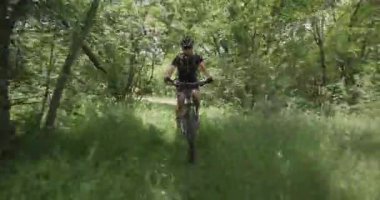 Yeşillik bir ormanda bisiklet süren bir adam. Doğadaki dağ bisikletçisi. Ön manzara. Sinema kamerasıyla kaydedildi..