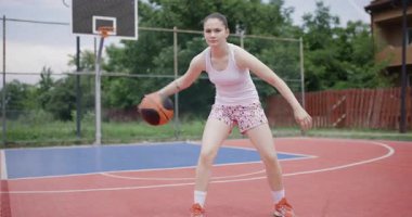 Atletizmi vurgulayan ve şehir ortamında odaklanan kararlı bir bayan basketbolcu açık havada kendinden emin bir şekilde salya akıtıyor..