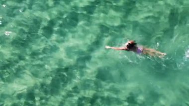 Bir kadın kristal berrak turkuaz suda yüzüyor. Bikinili bir kadının tatilinin tadını çıkardığı hava manzarası..