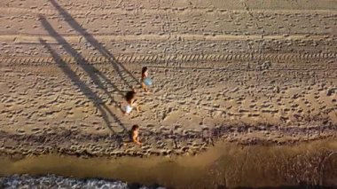 Kumsalda aile eğlencesi. Anne ve kız çocuklarının çıplak ayakla yürümeleri, deniz kıyısında güneşli bir günün tadını çıkarmaları..