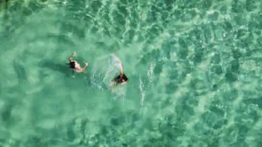 İki kadın kristal berrak turkuaz suda yüzüyor. Arkadaşların kumsaldaki yaz tatilinin keyfini çıkardıkları hava manzarası..