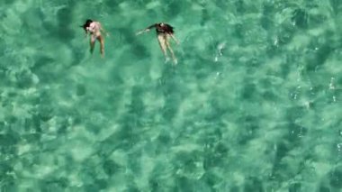 İki kadın, kristal berraklığında turkuaz suyun tadını çıkarıyorlar. Yaz tatilleri boyunca yüzeyde yüzüyor ve dinleniyorlar..