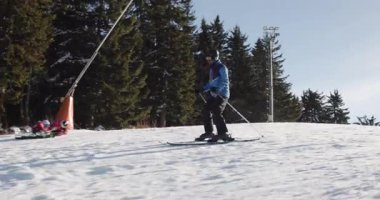 Bir kayakçı, açık gökyüzünün altında, daima yeşil ağaçlarla çevrili, karlı bir yamaçtan ustalıkla iner. Görüntü, kış sporlarının doğal ortamdaki heyecan ve güzelliğini somutlaştırıyor..