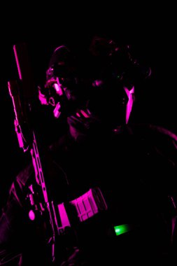 Koyu renk taktik teçhizatlı bir asker elinde pembe ışıkla vurgulanmış bir silahla görüntüde bir gizem ve yoğunluk hissi yaratır..