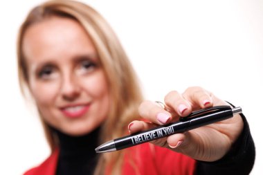 Bir iş kadını, elinde motive edici bir ifade olan bir kalem tutarken gülümser ve profesyonel bir ortamda pozitifliği ve teşvikleri yansıtır. Parlak arka plan kendine güveni arttırıyor..