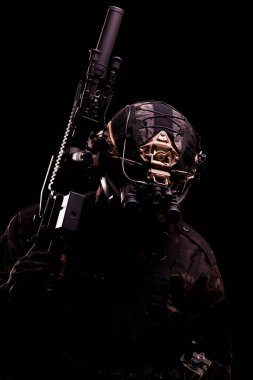 Bir askeri operatörün siyah portresi gelişmiş bir taktik ekipman ve ateşli bir silah giyiyor..