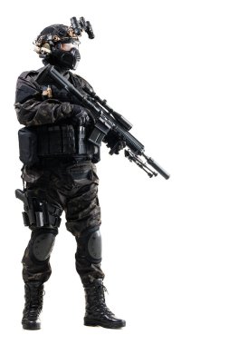 Siyah üniforma ve kask giyen, çeşitli teçhizatlarla donatılmış ve tüfeği hazır vaziyette duran bir taktik askeri. Rakamlar profesyonelliği ve hazırlığı ifade ediyor.