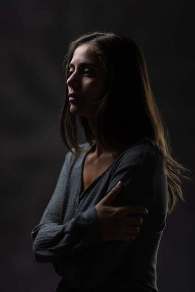 Студийный портрет молодой женщины с задумчивым выражением лица, снятый при ярком боковом освещении на сером фоне.
