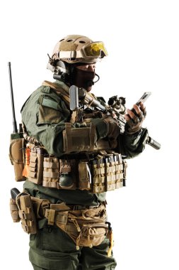 Tam teçhizatlı bir taktik operatörü, gelişmiş askeri teçhizat ve koruyucu miğferle donatılmış bir akıllı telefon tutuyor, modern savaş teknolojisi ve iletişimi gösteriyor..