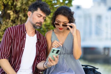 Güneşli bir günde, dışarıda birlikte oturan genç bir çift akıllı telefona bakarken bir anı paylaşıyorlar. Sahne bağlılık ve bağlılık taşır.