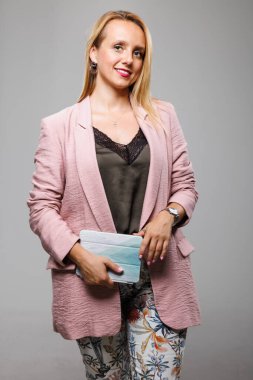 Şık bir ceket ve çiçekli pantolon giymiş kendine güvenen bir kadın gülümserken debriyajı tutuyor. Ayarlar modern bir iç mekan olduğunu gösteriyor, muhtemelen şahsi bir marka çekimi için..