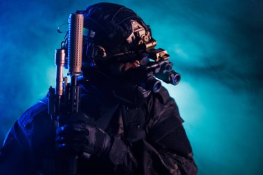 Gelişmiş silahlar taşıyan, gece görüş teknolojisi kullanan, etkileyici bir arka planı olan bir özel kuvvetler askerinin silüeti. Askeri hassasiyeti, gelişmiş taktikleri ve işlevselliği temsil eder.