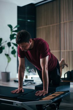 Bir adam, iyi ışıklandırılmış, çağdaş bir stüdyo ortamında güç ve denge sergileyen, yenilikçi bir pilates makinesinde zorlu bir antrenmana girişir..