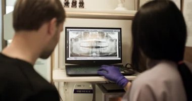 Bir hemşirenin hastaların röntgenlerini bilgisayarda incelediği bir diş muayenehanesi. Görüntü diş bakımı, muayene ve profesyonel sağlık hizmetlerine odaklanmayı vurgular.