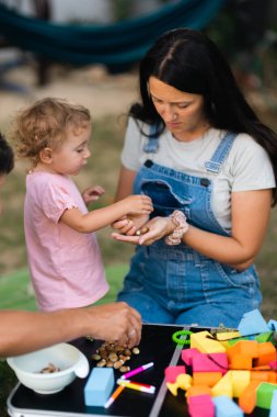 Şefkatli bir anne küçük kızıyla açık hava ortamında renkli oyuncaklar ve doğal malzemeler kullanarak oyun yoluyla öğrenmeyi teşvik eder. Aile bağı ve erken çocukluk gelişimi.
