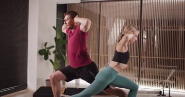 İki birey, esneklik ve dengeyi vurgulayarak bir çift yoga seansına katılıyor. Modern stüdyo, hafif ışıklandırma ve yeşilliklerle, egzersizleri için rahatlatıcı bir atmosfer yaratıyor..