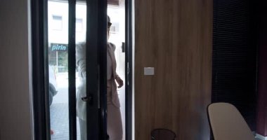 Şık giyinmiş bir kadın kalabalık bir şehir bölgesinde lüks bir kaplıcaya açılan kapıyı açıyor. Ayar parlak, profesyonellik ve rahatlama karışımı bir şey sergiliyor..