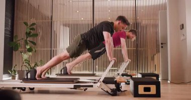 Parlak ve ferah bir stüdyoda, iki birey reformcu makineler kullanarak odaklanmış bir pilates seansına girişiyor. Güç ve esnekliği artırma amaçlı çeşitli egzersizler sergiliyorlar..