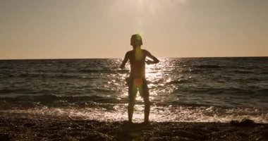 A striking silhouette of a young child celebrating freedom and hope on a tranquil beach as the sun sets over the glistening ocean waves, hands raised in triumph.